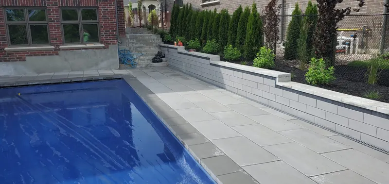 Block retaining wall with cap stones holding the grade beside a pool deck