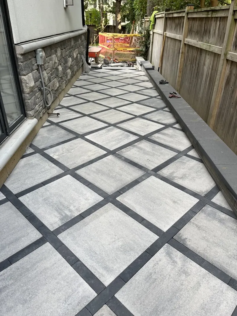 Side-yard interlock walkway laid in a diamond pattern with charcoal banding