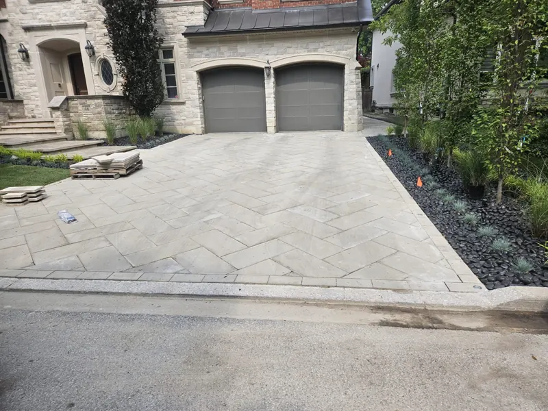 Finished herringbone interlocking driveway with a soldier-course border in front of a stone house