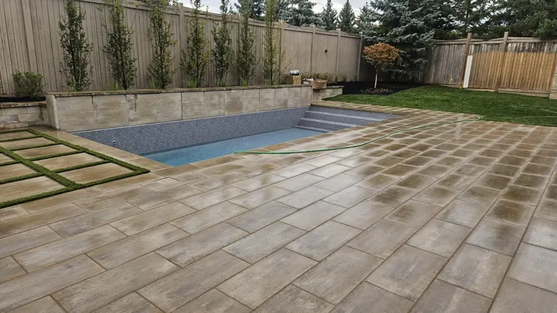 Raised planter wall with columnar trees behind a large-format pool deck